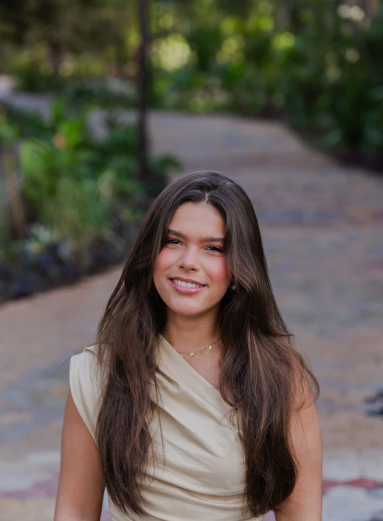 A smiling young woman with long brown hair on a garden path