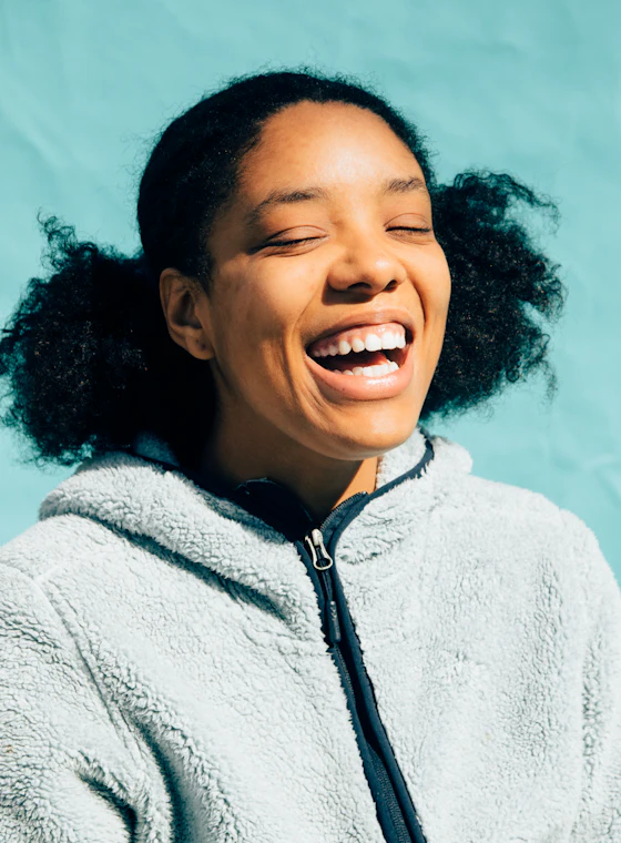 A young woman in a fleece jacket laughing in front of a teal wall